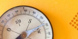Close-up of a vintage compass pointing southwest, set against a bright yellow background with orange dots—perfect for those feeling lost without BoardBooster. Here’s how to succeed on Pinterest with Tailwind as your guide.