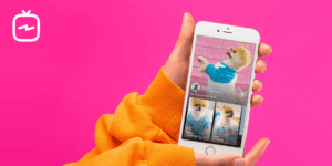 A person in an orange sweater holds a smartphone, showing videos of a small dog in different outfits. A white Instagram TV logo in the top left highlights how IGTV for marketers can be used to share creative content. The background is bright pink.