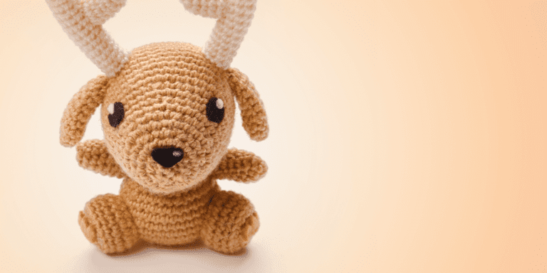 A crocheted stuffed animal resembling a deer, with tan and white yarn, large black eyes, and small antlers, sits against a soft beige background—perfect inspiration if you’re looking up how to pin Etsy items on Pinterest.