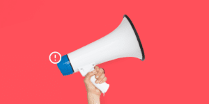 A hand holding a white megaphone with a blue speaker against a solid pink background, symbolizing how to report stolen pins on Pinterest, with a small exclamation mark icon near the megaphone.