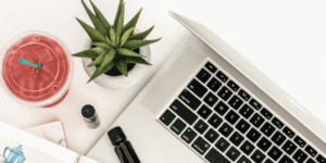 A top-down view of a laptop keyboard next to a potted succulent, a red iced drink with a green straw, a small essential oil bottle, and part of a notebook—perfect for planning the one thing you can do to increase Pinterest traffic.