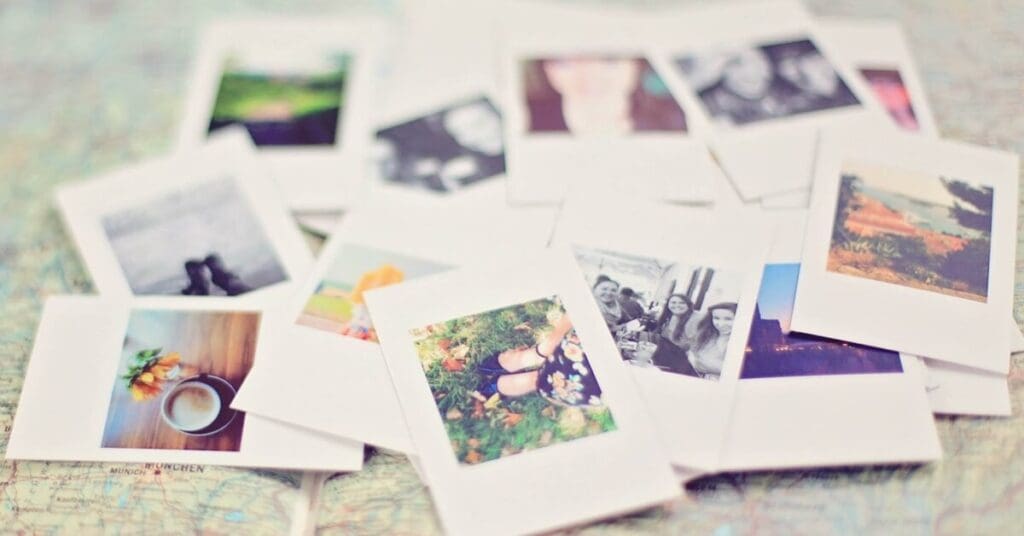 A scattered pile of instant photo prints, reminiscent of instagram image resources, displays colorful images of landscapes, people, and objects laid out on a blurred map background.