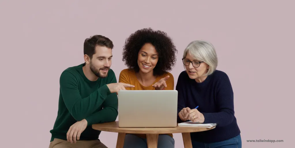 Three people of different ages sitting at a round table, smiling and pointing at a laptop, representing sharing Pinterest boards.