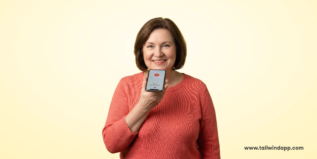 Woman in orange sweater holding a smartphone, smiling at the camera.